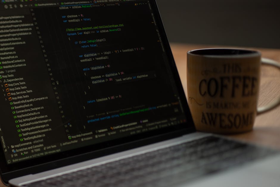 A close-up view of a laptop displaying lines of programming code, with a white coffee mug positioned in the background on a wooden surface. The mug features text related to coffee, emphasizing a relax