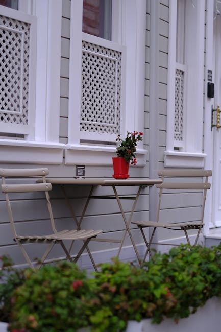 A close-up view of a quaint front garden in a period home in Camden Town, featuring a white-painted wooden exterior with decorative lattice panels below the windows. A small, rectangular folding table