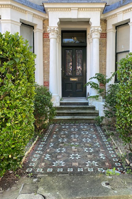 A close-up view of a quaint front garden in a period home in Camden Town, featuring a white-painted wooden exterior with decorative lattice panels below the windows. A small, rectangular folding table